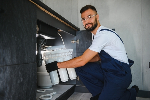 Plumber in blue overalls and gloves working under a sink, demonstrating local plumbing services and expertise.